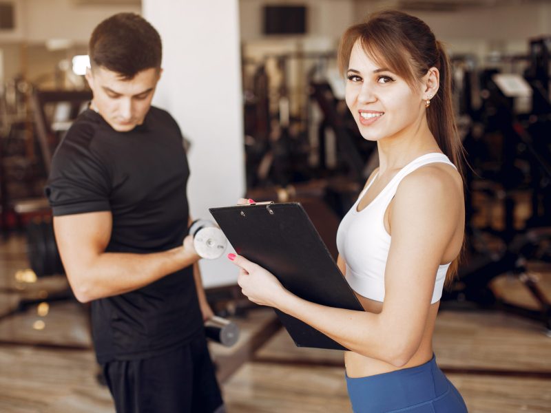 Couple in the gym. A woman performs exercises. Man in a black t-shirt